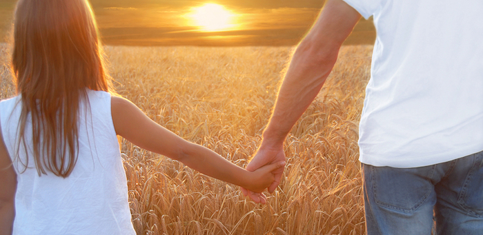 Father holding hands with his daughter at sunset in barley field