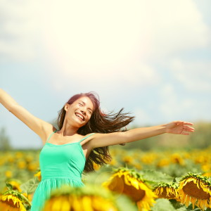 Happy woman in sunflower field. Summer girl in flower field cheerful and joyful. Multiracial Asian Caucasian young woman dancing, smiling elated and serene with arms raised up.